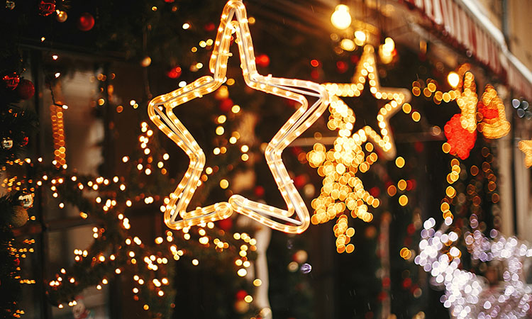 Stylish christmas golden star illumination and fir branches with red and gold baubles, golden lights bokeh on front of building at holiday market in city street. Christmas street decor