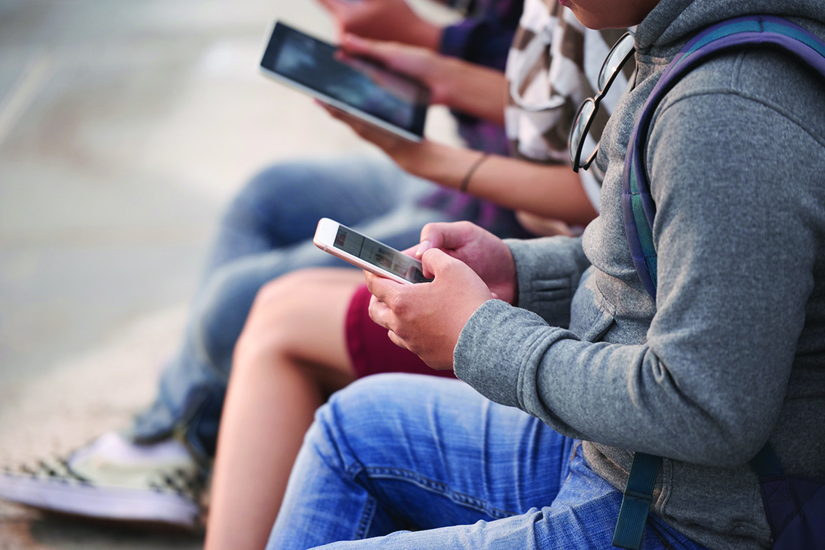 Unrecognizable group of friends in casualwear gathered together outdoors and using their devices, close-up shot